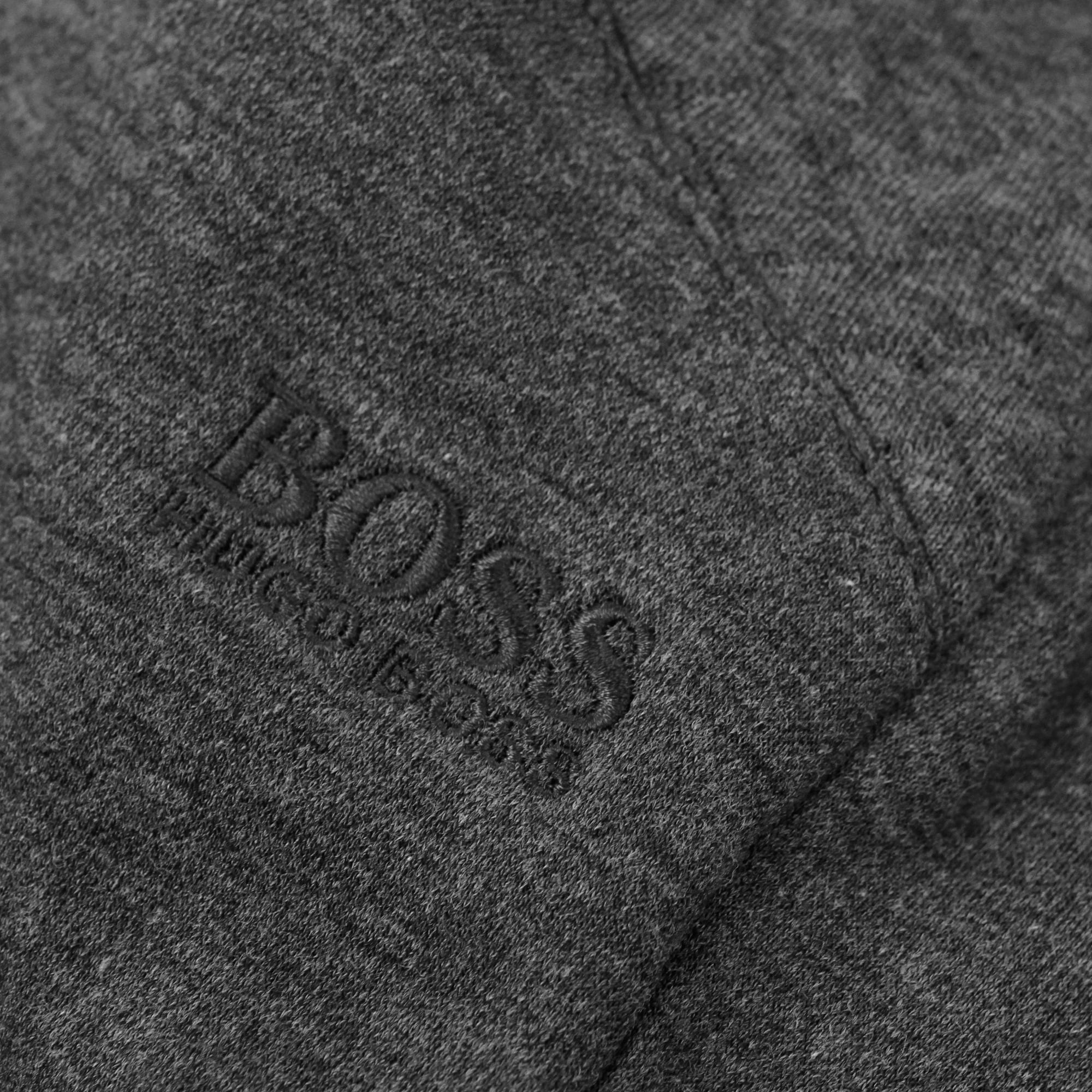 Close-up of the BOSS logo embroidered on the leg of dark grey track trousers.