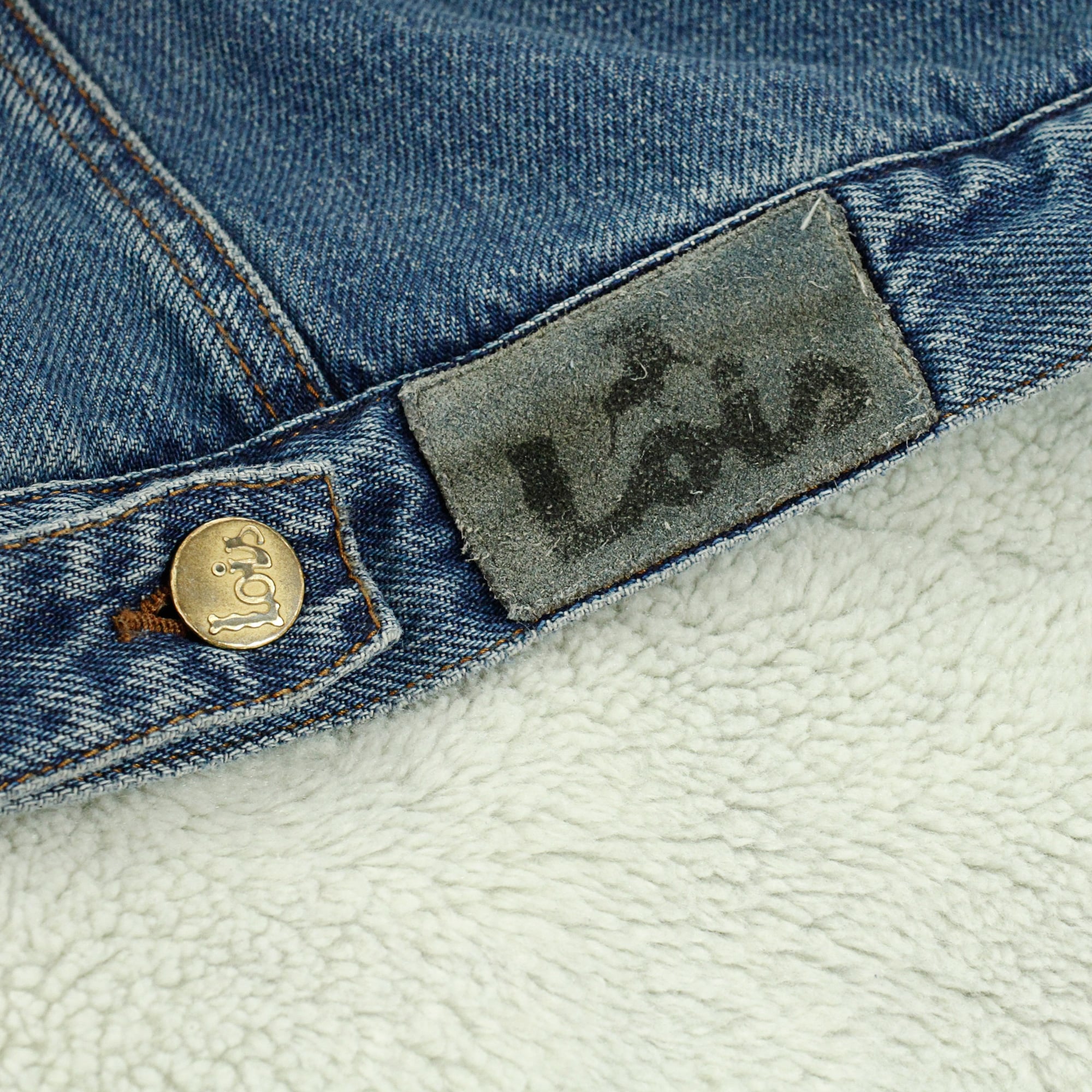 A close-up of the brand patch and stud detail on the jacket, with the fleece lining visible.