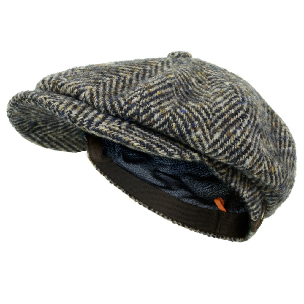 A grey and brown herringbone tweed flat cap, angled to show its brim and comfortable lining.