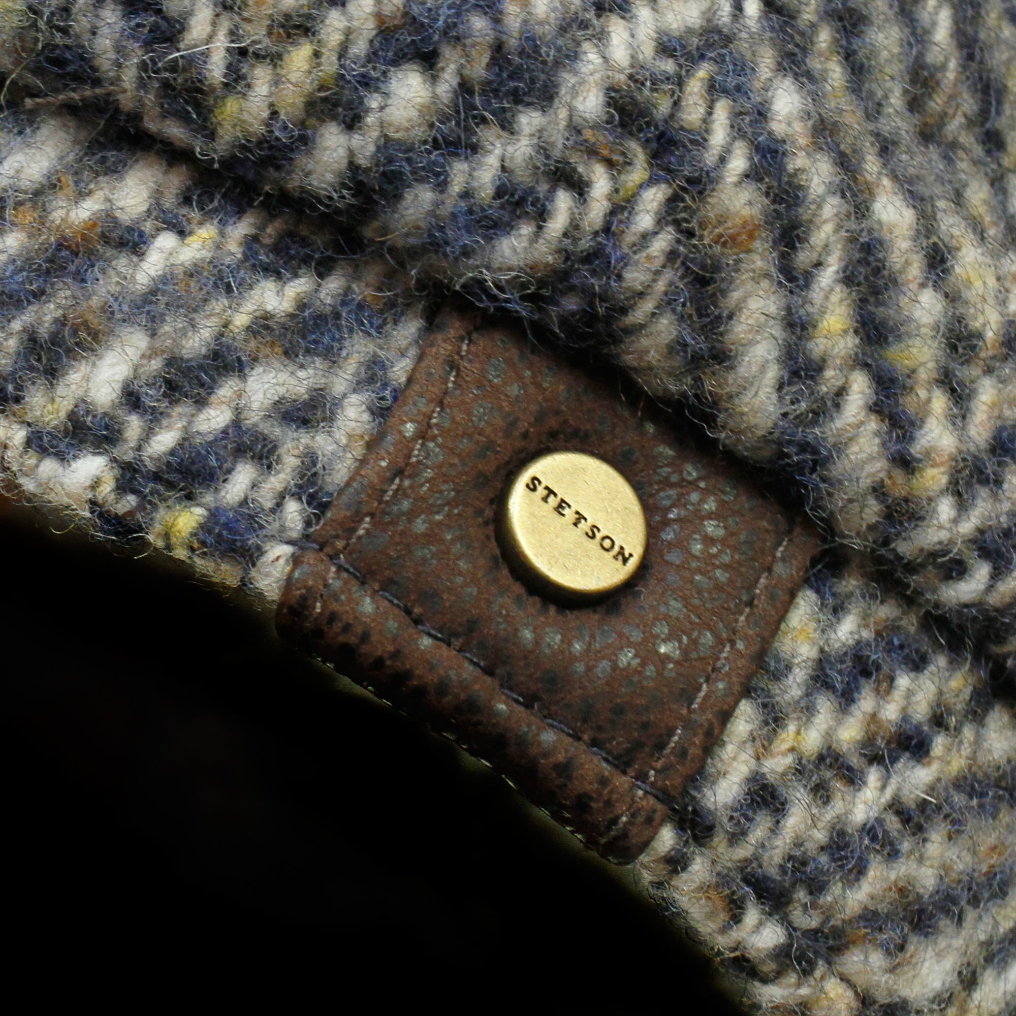 Close-up of a brown leather patch with a gold 'STETSON' button on a tweed cap.