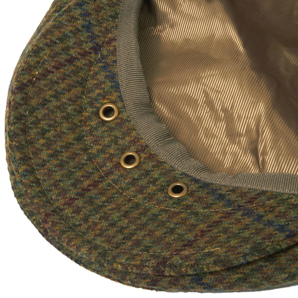 Close-up of the underside of an olive checked flat cap, showing eyelets and lining.