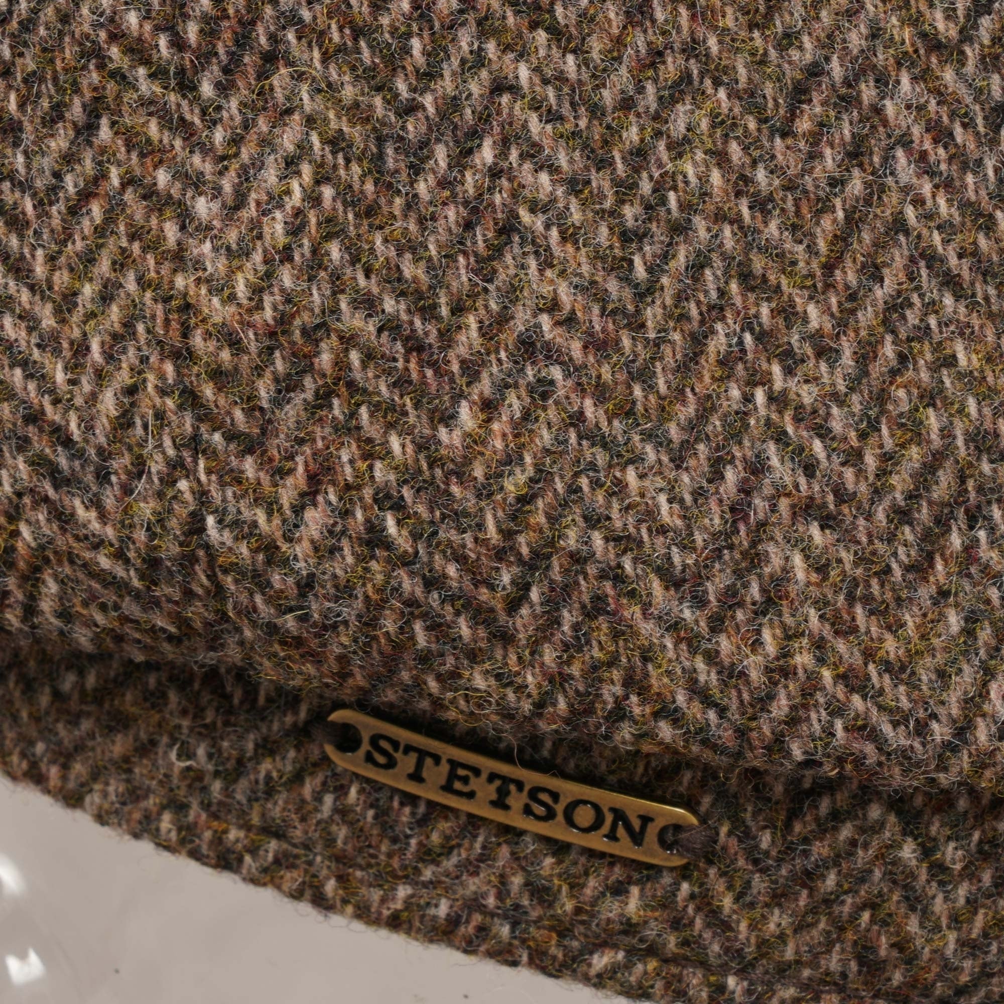 Close-up of the Stetson logo on the side of the brown herringbone flat cap.