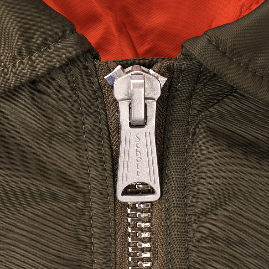 Close-up of the zipper on a khaki bomber jacket, showing the Schott logo.