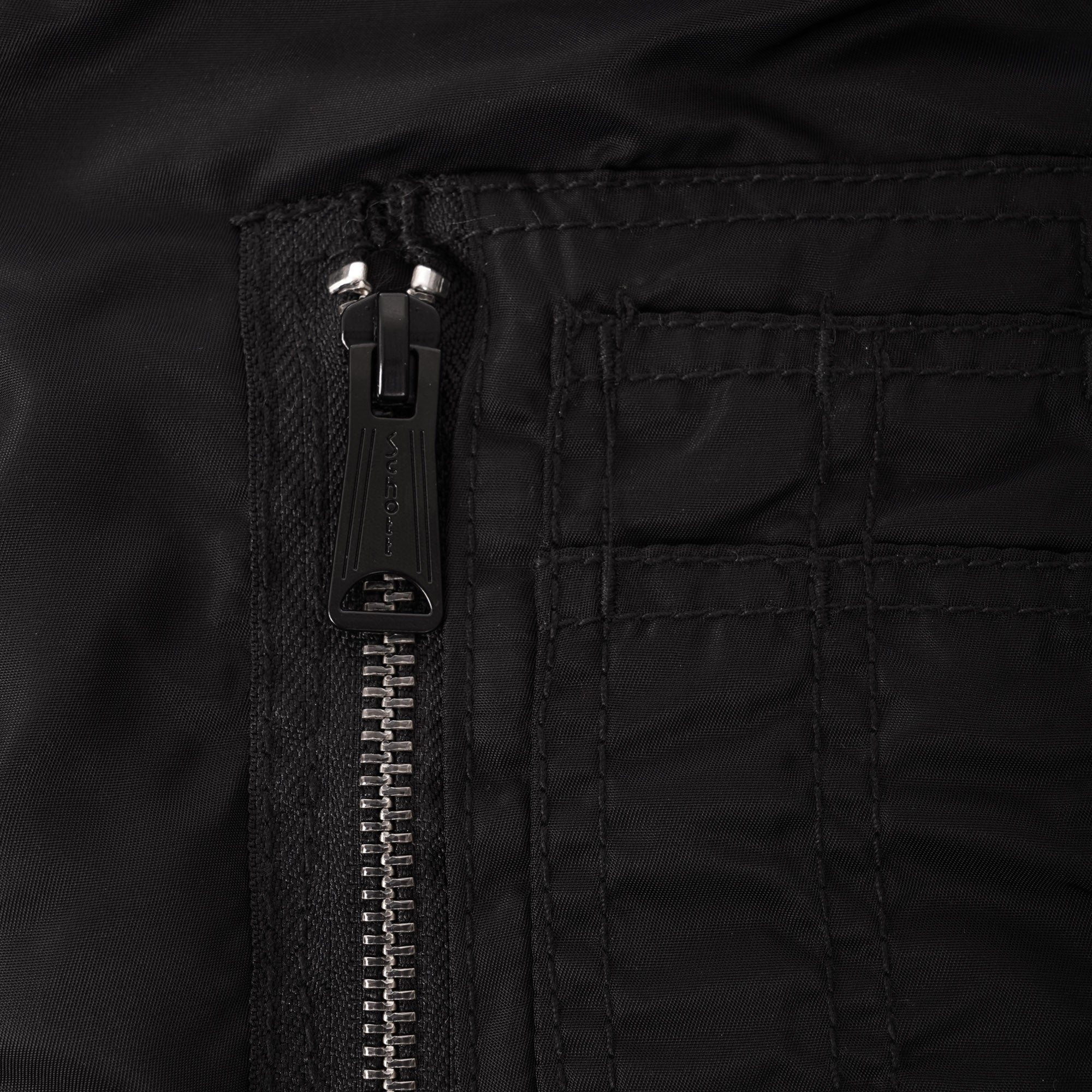 A close-up of a silver zip detail on a black jacket, showing the fabric texture.
