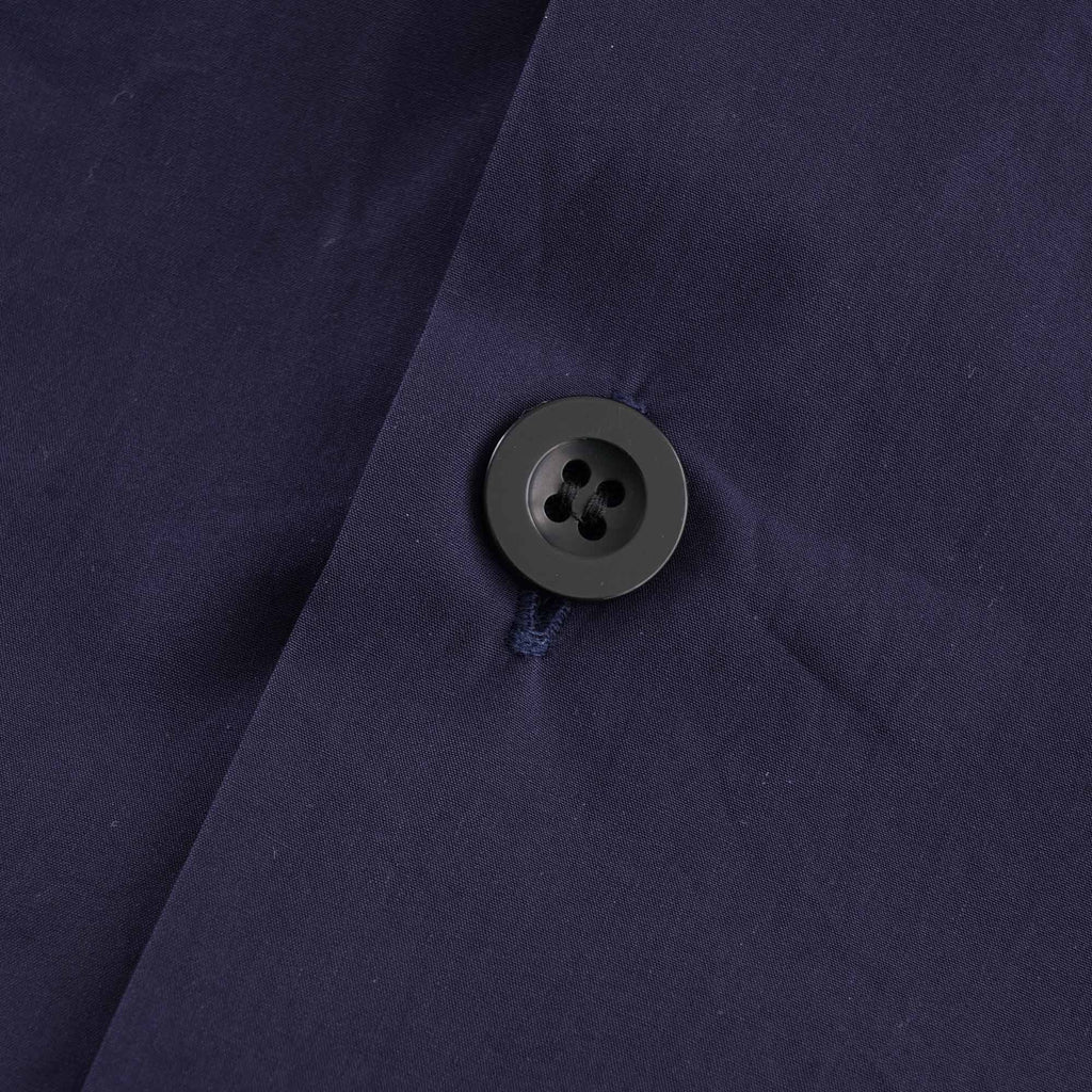 Close-up of a single dark grey button on the navy blue shirt fabric.