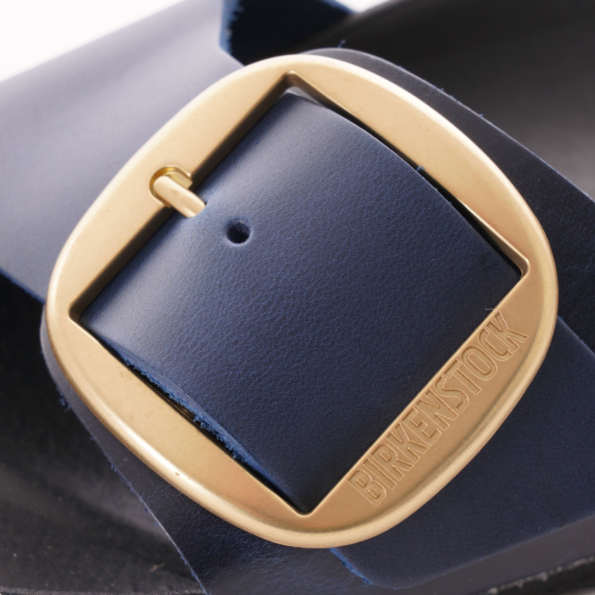 Close-up of the gold Birkenstock buckle on a navy blue sandal strap.