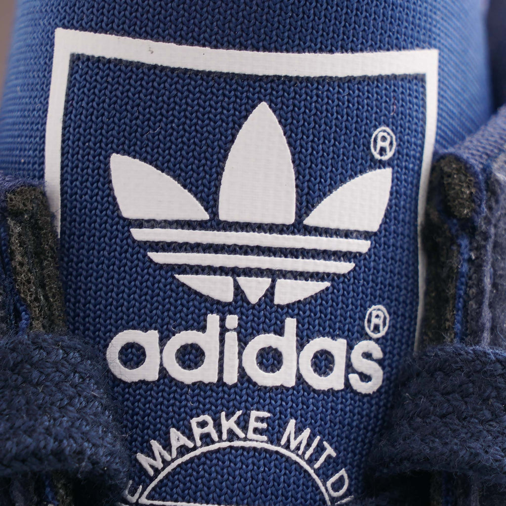 The Adidas logo on the tongue of a navy blue TRX Soulround trainer.
