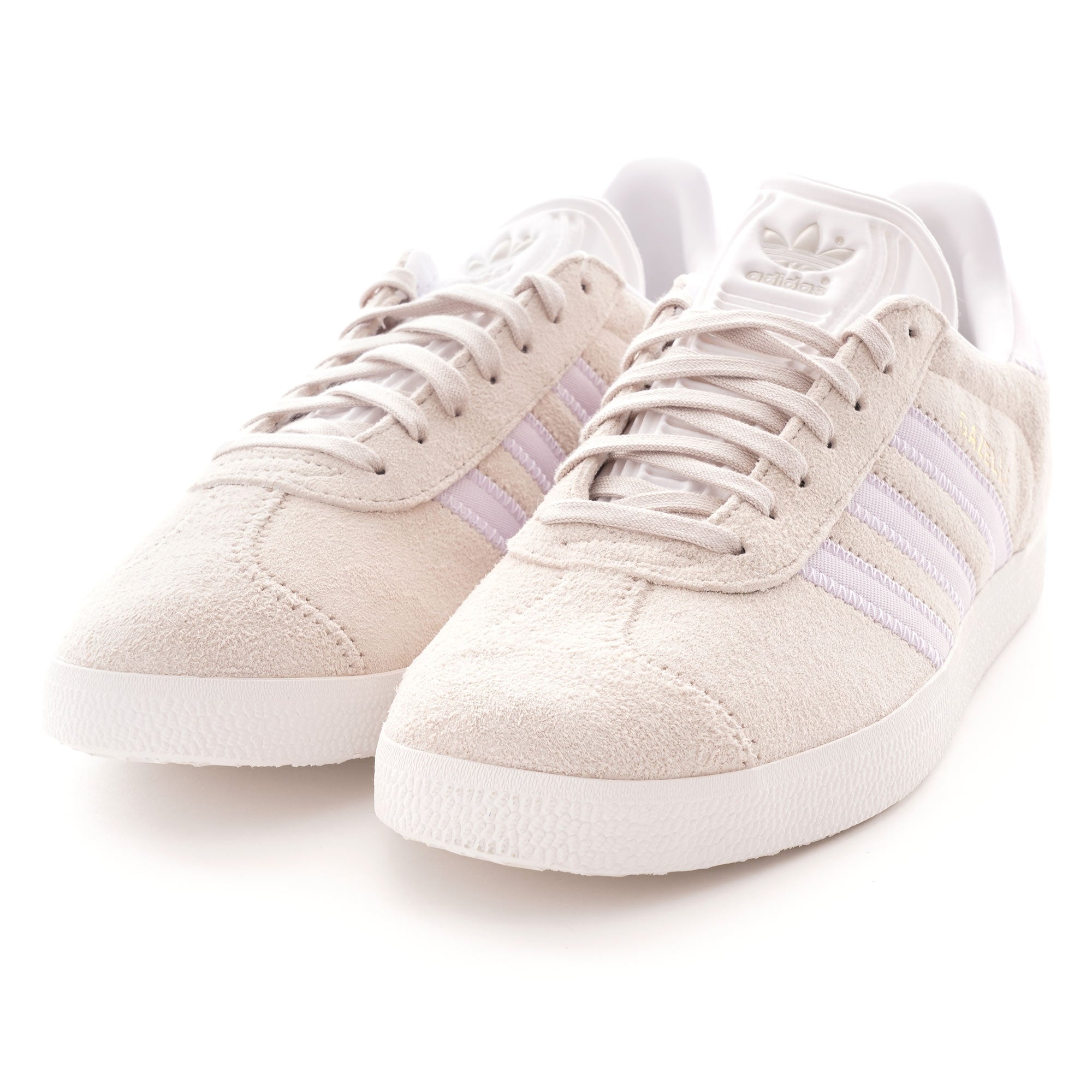 Two pale beige Adidas Gazelle trainers with three light purple stripes on the sides.