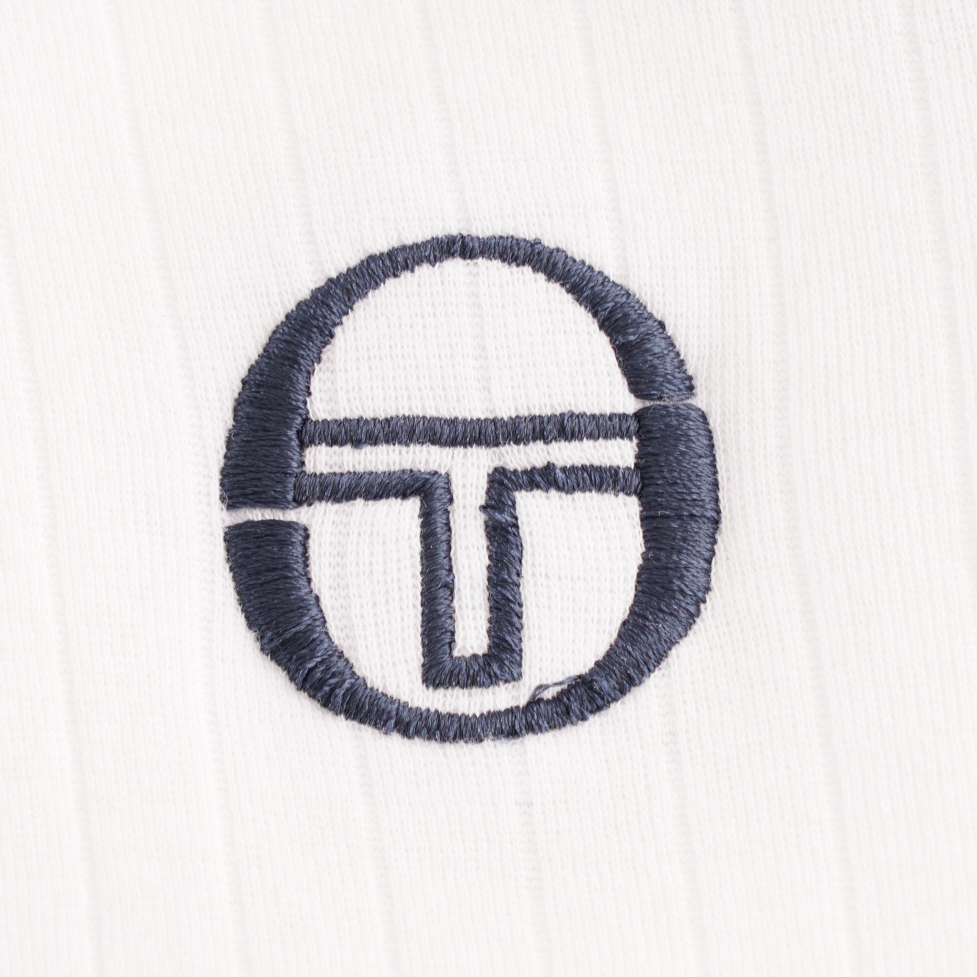 A detailed close-up of the embroidered navy brand logo on the white polo shirt.