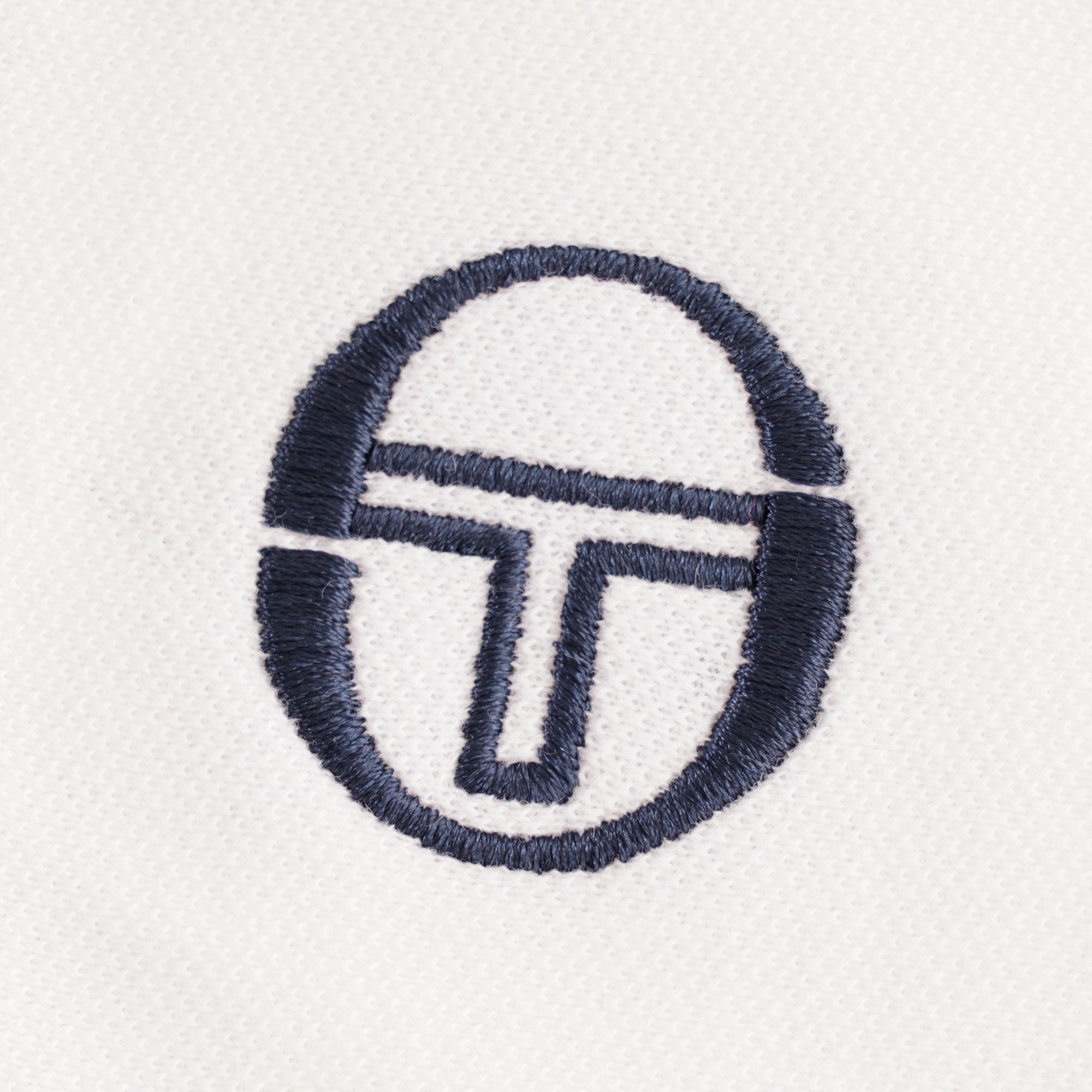 Close-up of the navy embroidered brand logo on the white polo shirt.