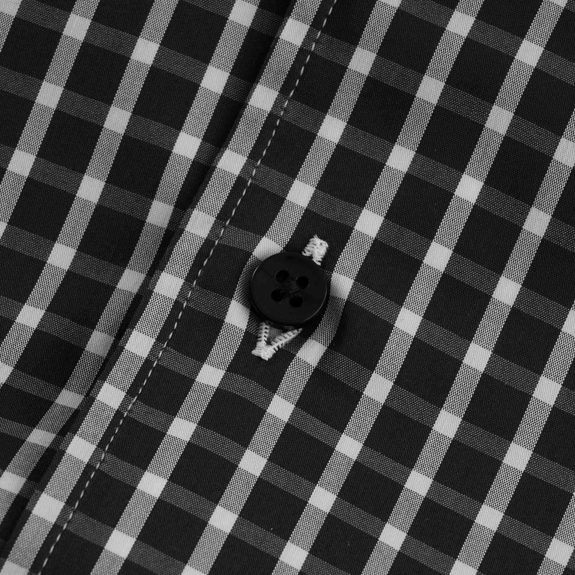 A close-up of a black button and stitching on the checked shirt.