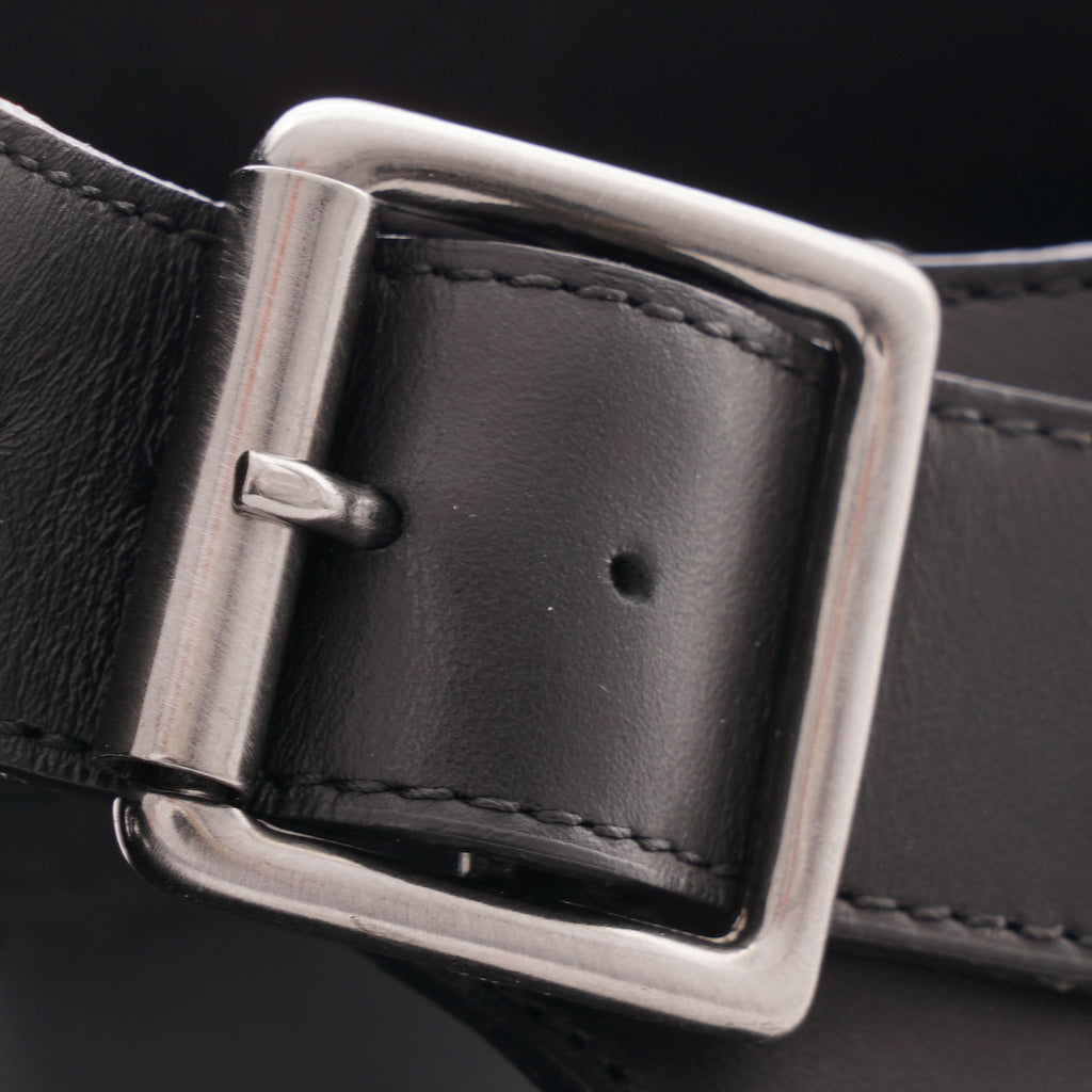 A close-up view of the silver-tone buckle and black leather strap of a sandal.