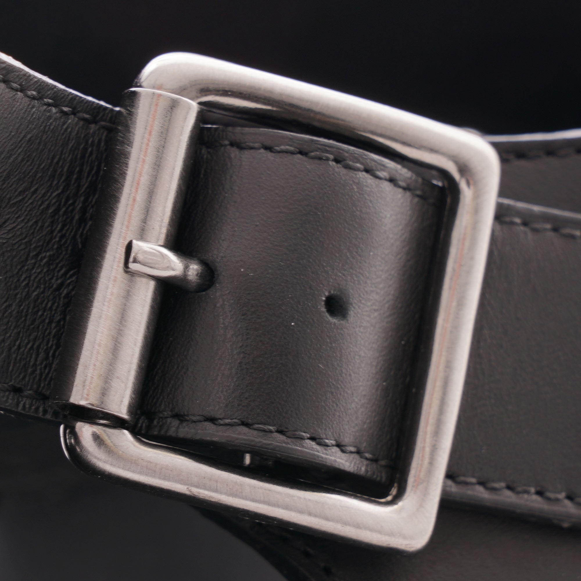A close-up view of the silver-tone buckle and black leather strap of a sandal.