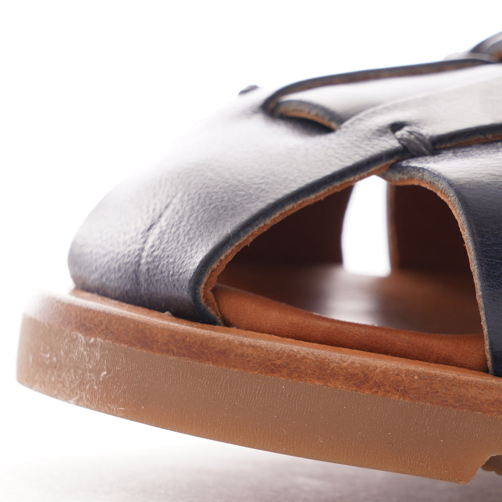 A close-up view of the toe of a dark blue leather fisherman's sandal with a brown sole.