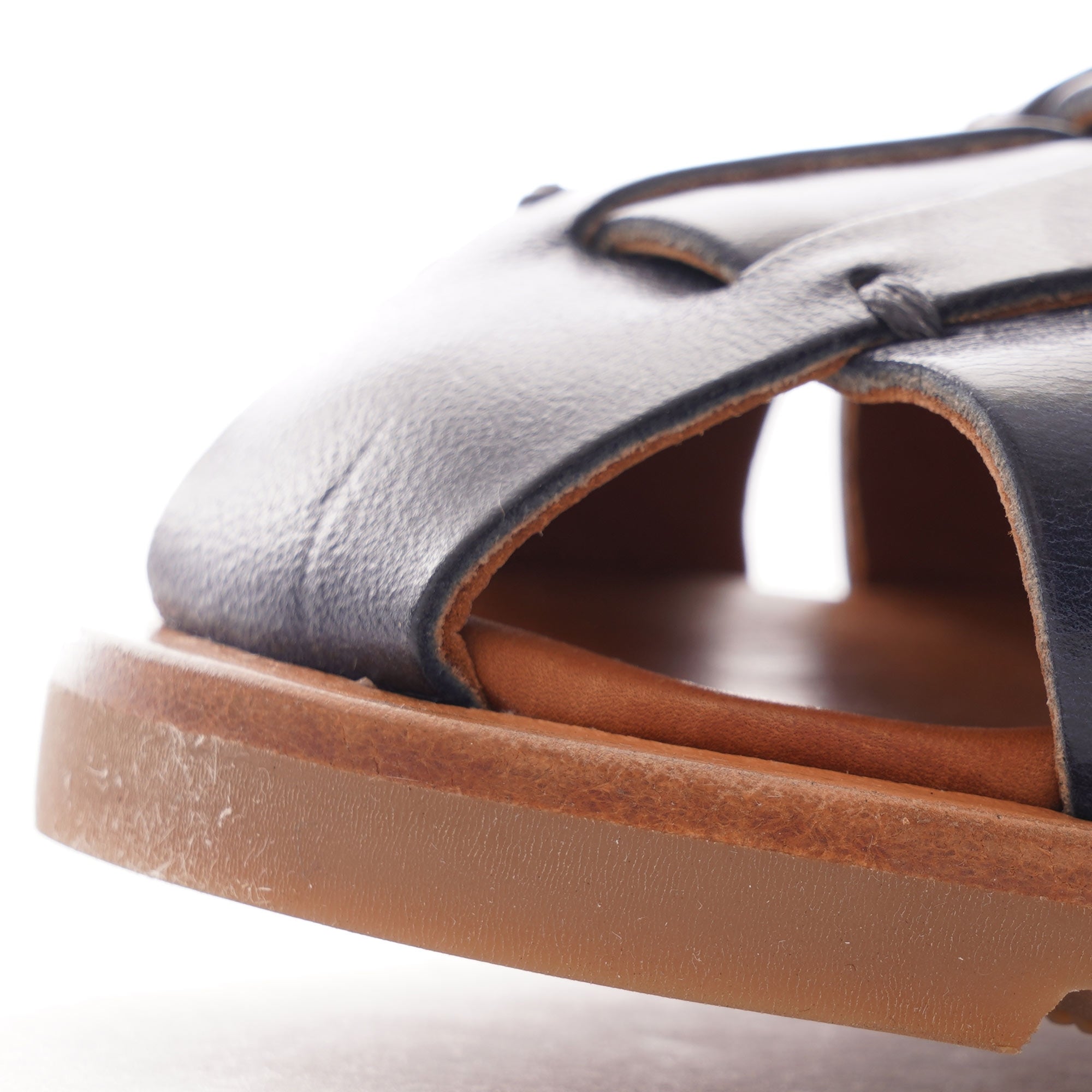 A close-up view of the toe of a dark blue leather fisherman's sandal with a brown sole.