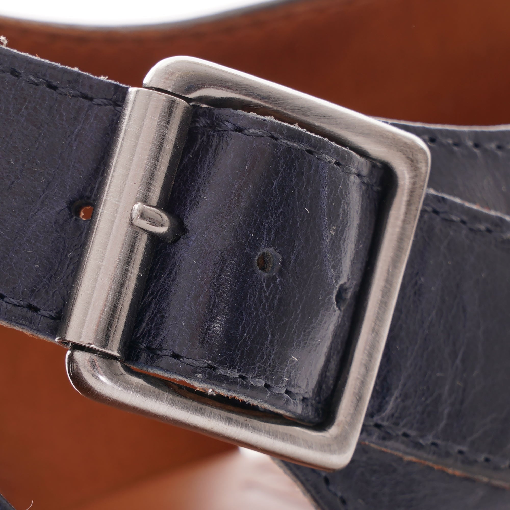 A close-up view of the silver buckle on a dark blue leather fisherman's sandal.