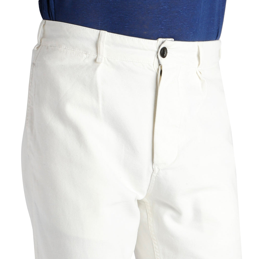 A close-up of the waist and fly of the white trousers, worn by a person in a navy top.