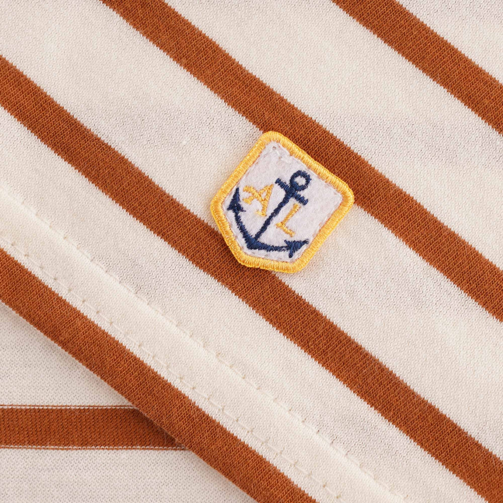 Close-up of the embroidered Anchor Lux logo patch on a striped t-shirt.