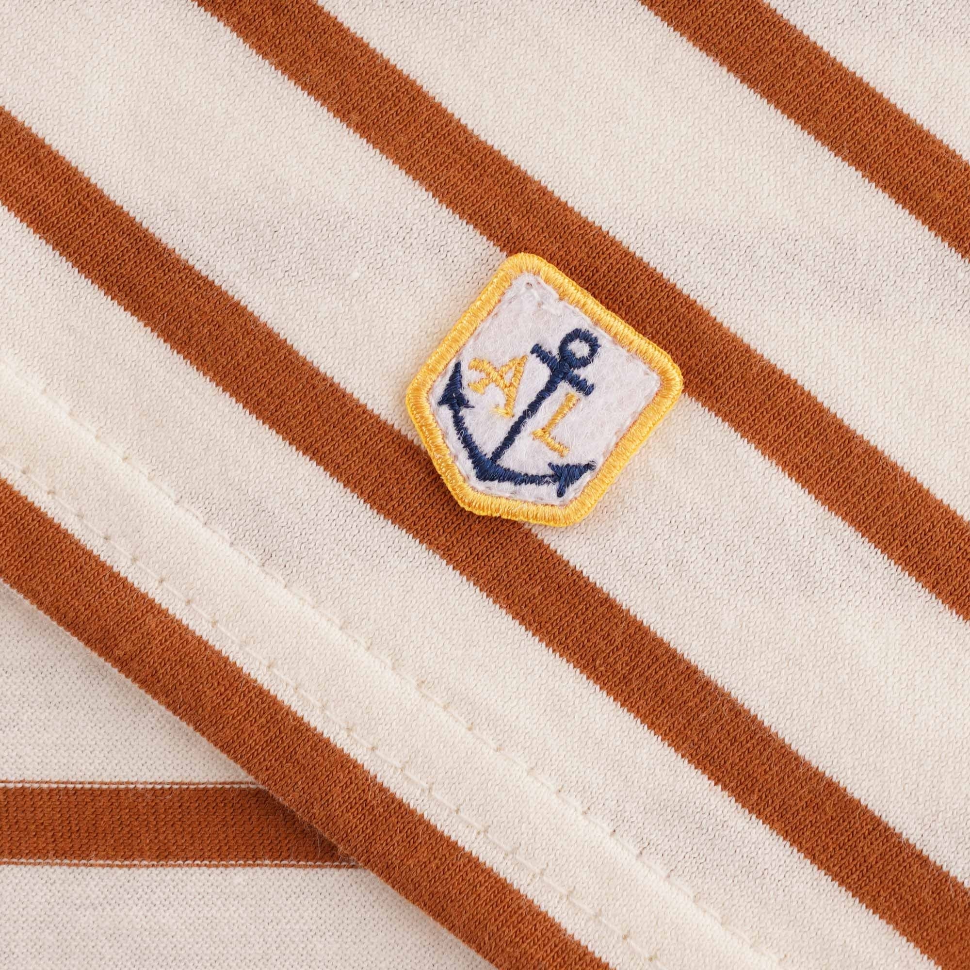 Close-up of the embroidered Anchor Lux logo patch on a striped t-shirt.