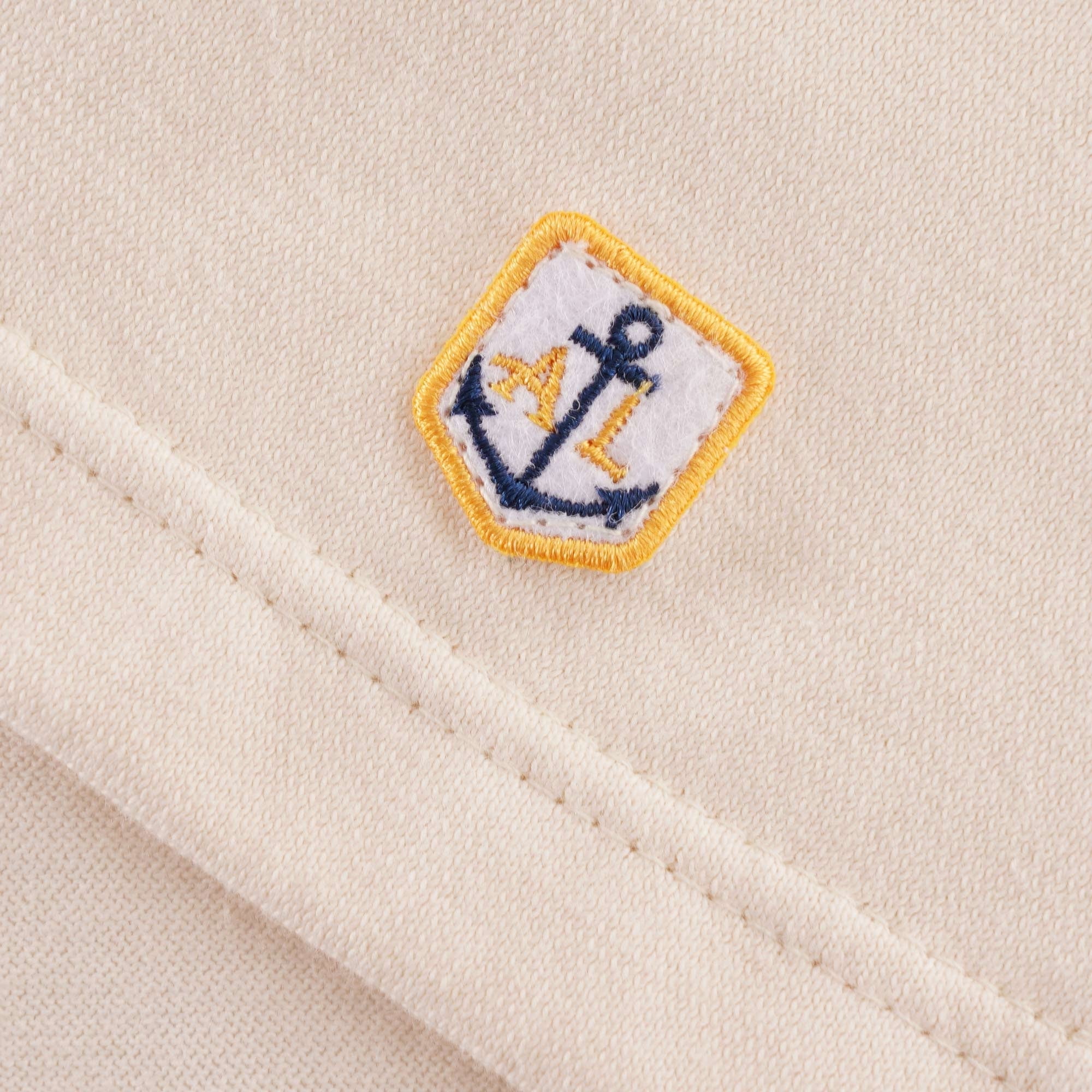A detailed view of the small anchor logo on the bottom hem of the Loctudy T-Shirt.
