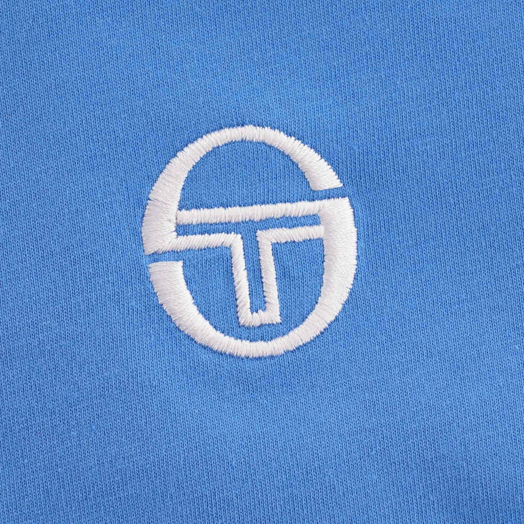 Close-up of the Sergio Tacchini logo embroidered on the blue t-shirt.