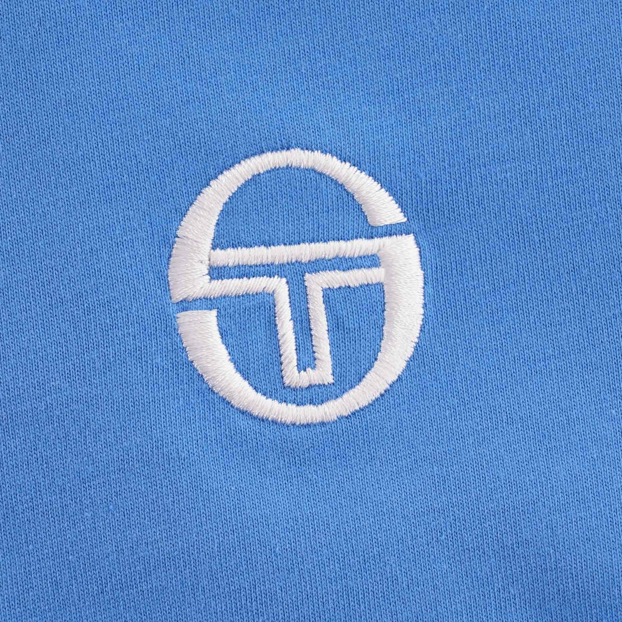 Close-up of the Sergio Tacchini logo embroidered on the blue t-shirt.
