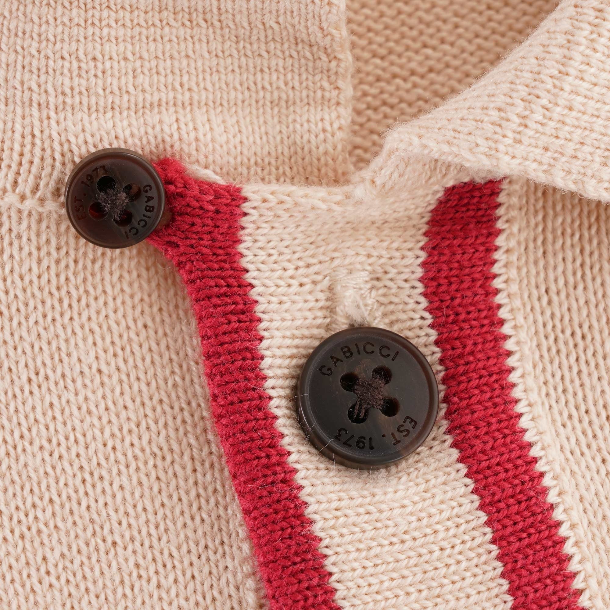 A close up of the buttons on a beige polo shirt with a red trim.