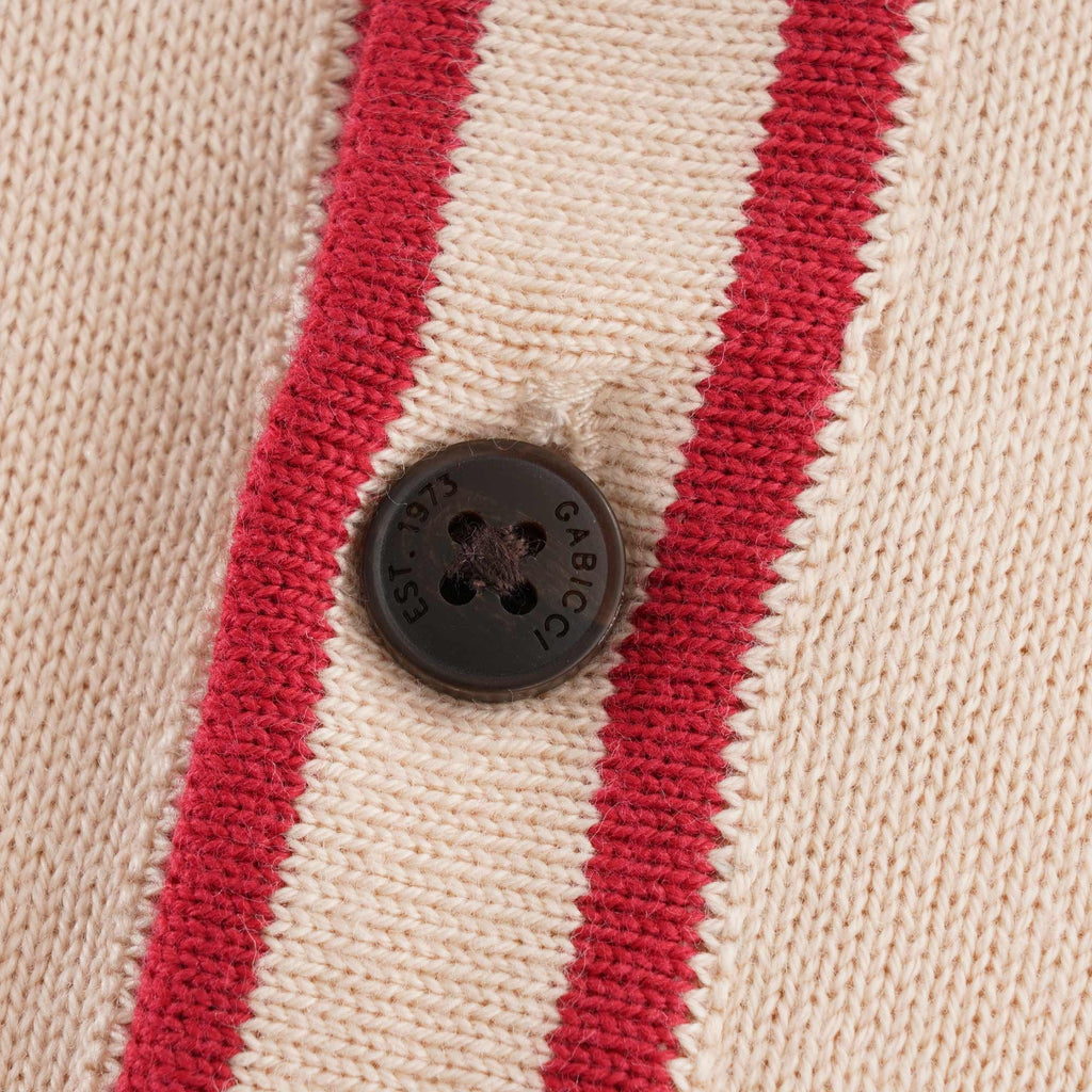 A close up of a single button on a beige polo shirt with a red trim.