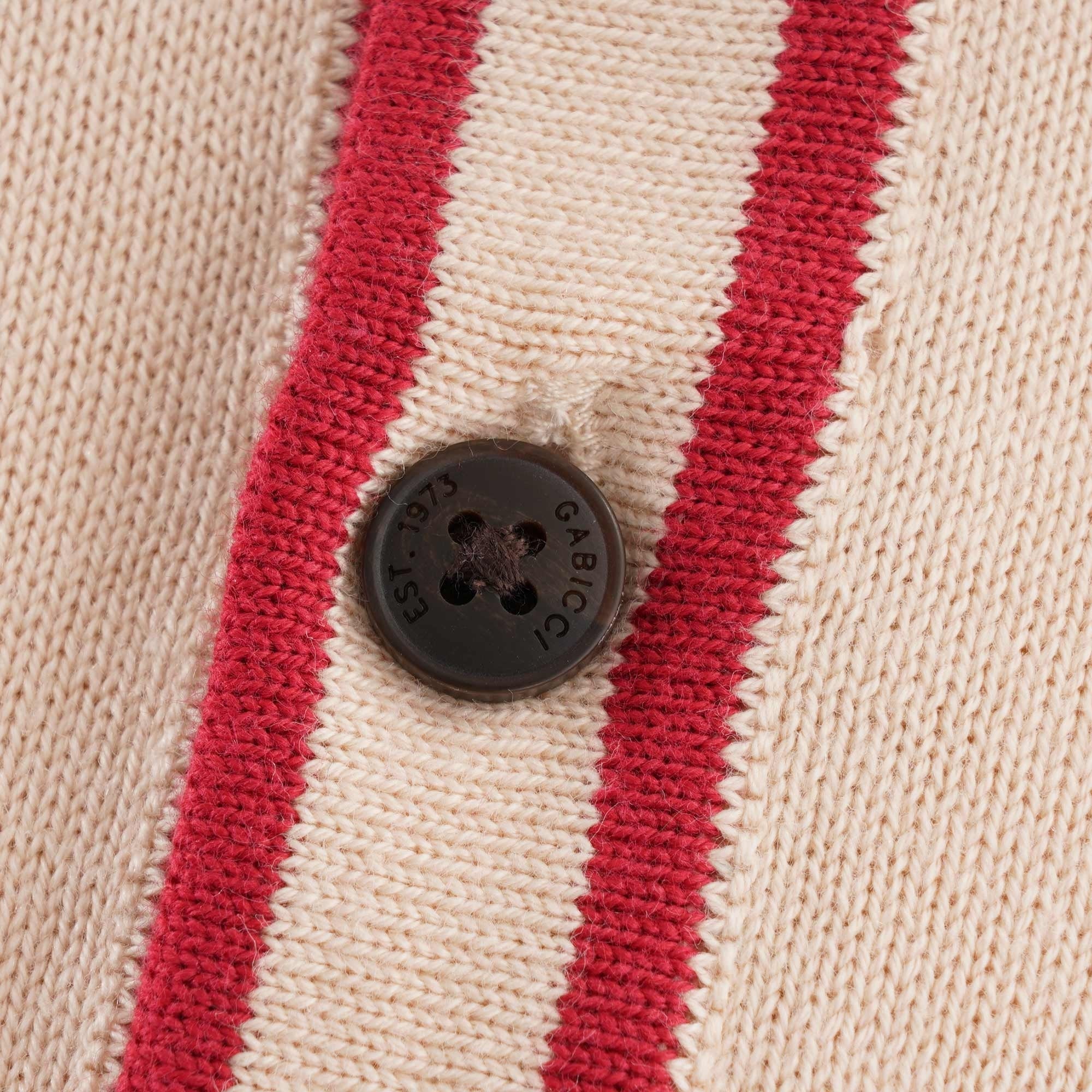 A close up of a single button on a beige polo shirt with a red trim.