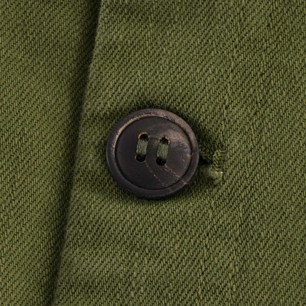 Close-up of a dark, textured button on an olive green fabric.