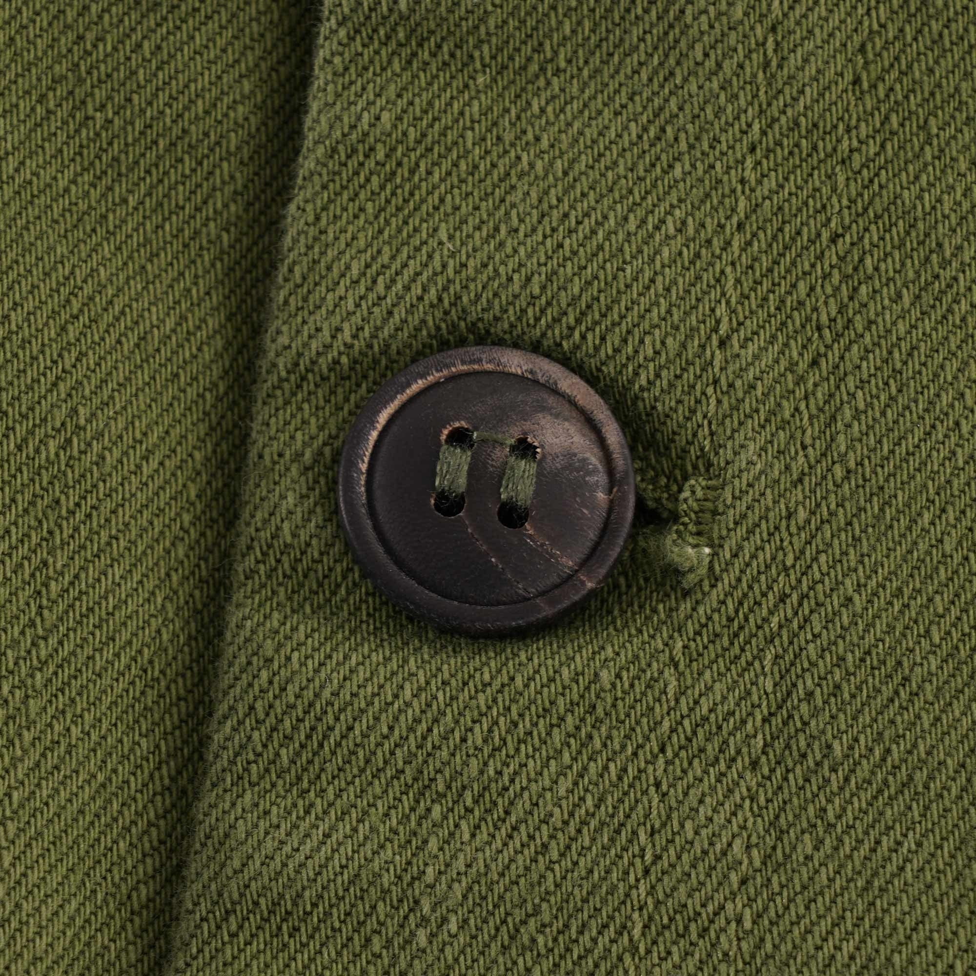 Close-up of a dark, textured button on an olive green fabric.