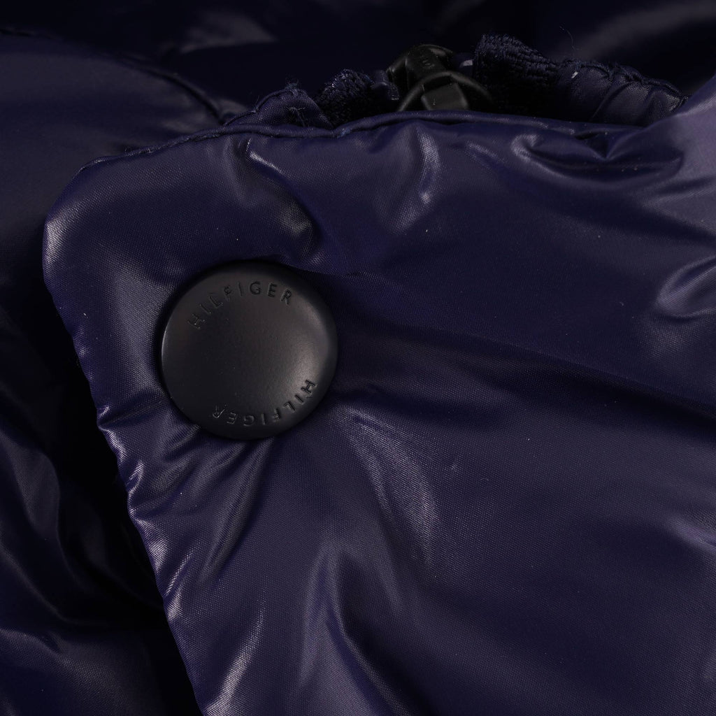 A close-up of a dark button with 'HILFIGER' text on the navy blue puffer jacket.