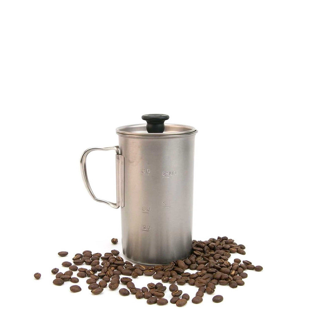 A stainless steel travel coffee press stands on coffee beans against a white background.