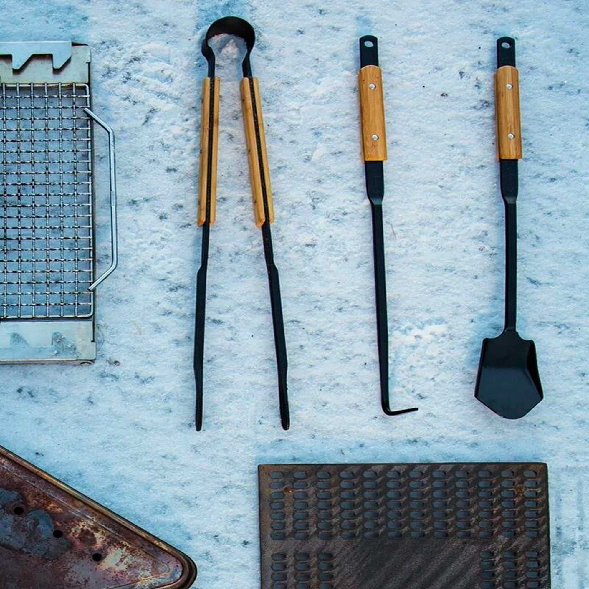 Snow Peak barbecue tools: tongs, poker, and spatula laid out on a stone surface.