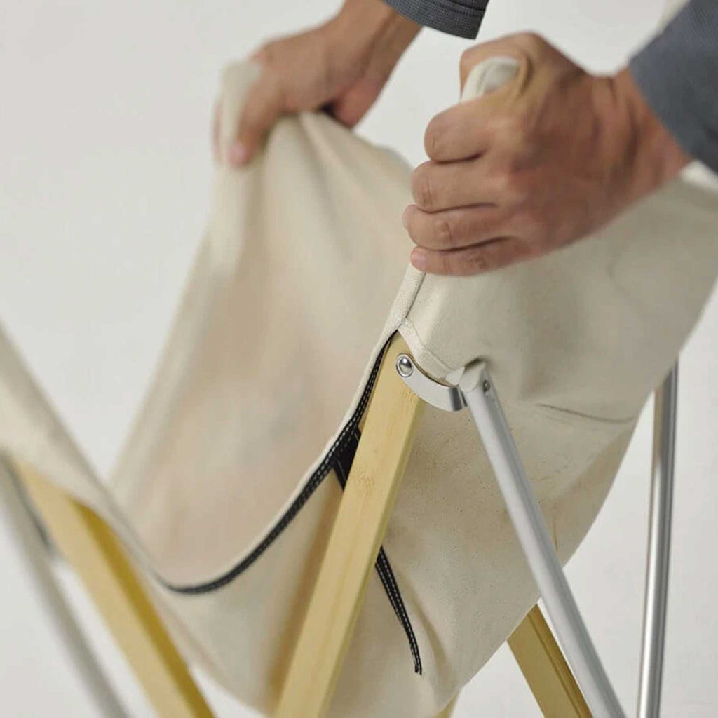 Hands demonstrating how to fold the chair by pulling the canvas seat upwards.