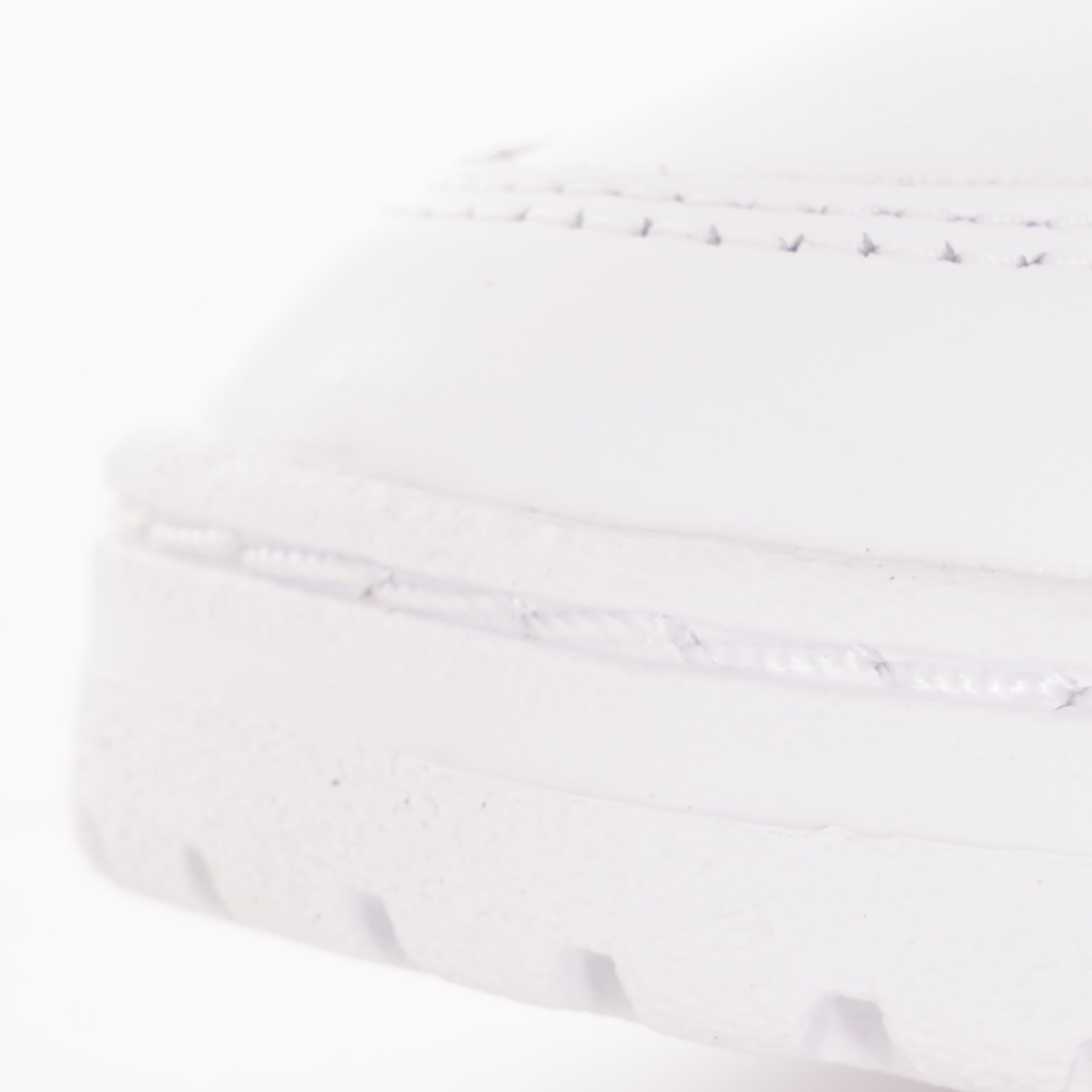 A close-up of the textured toe-cap of a white Adidas trainer with blue and red stripes.