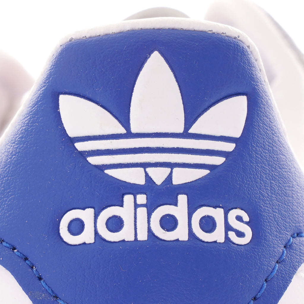 A close-up of the blue Adidas logo on the heel of a white Adidas trainer.