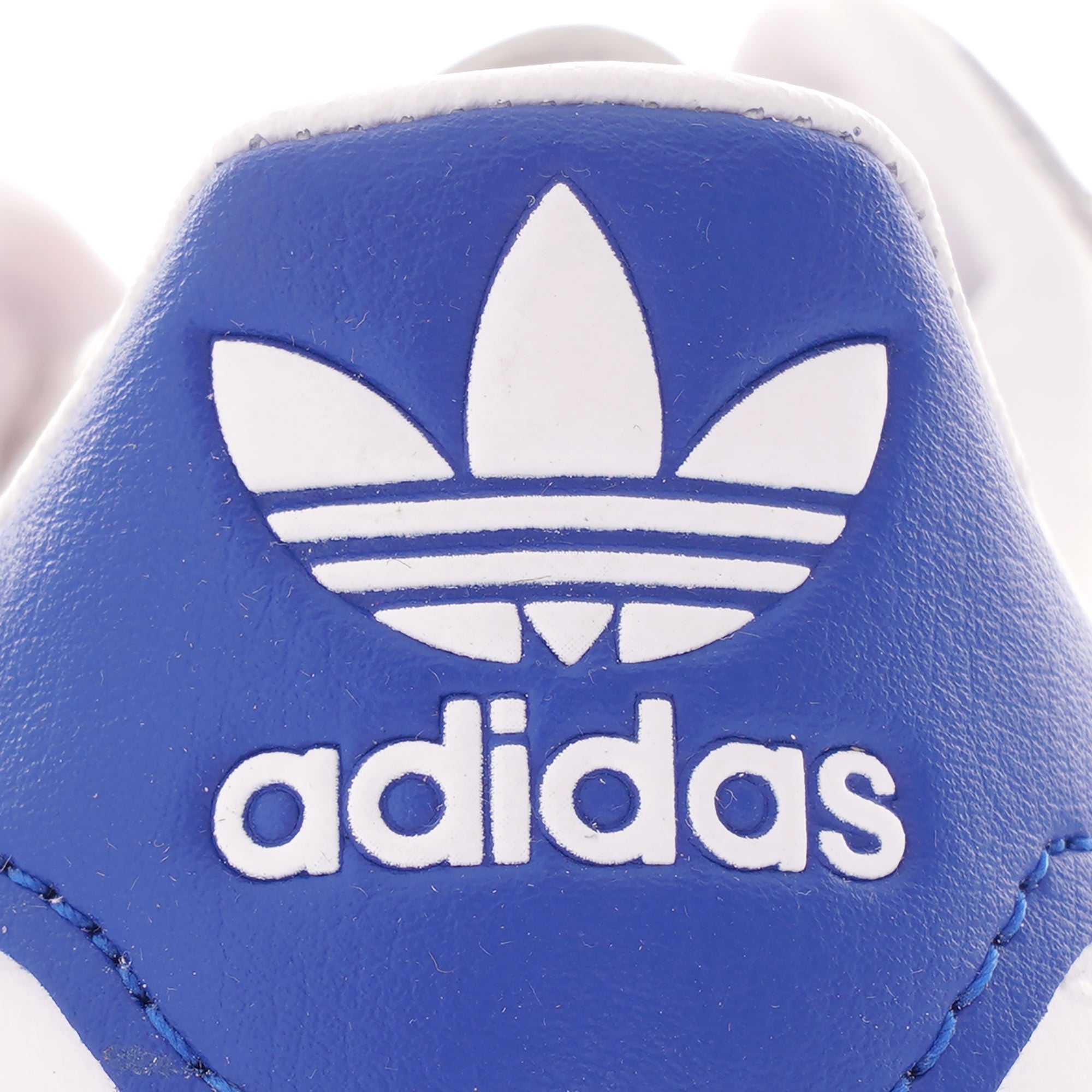 A close-up of the blue Adidas logo on the heel of a white Adidas trainer.