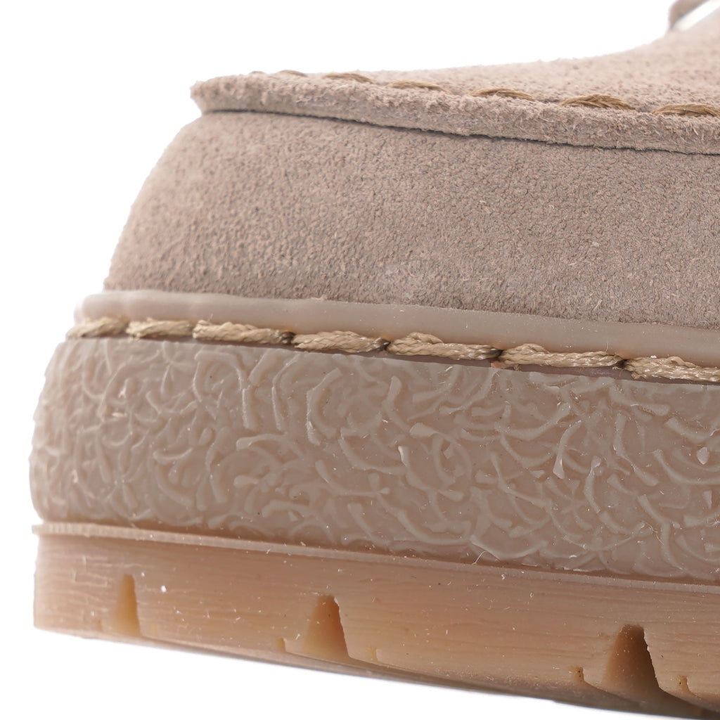 A close-up of the textured rubber sole and suede stitching on a beige shoe.