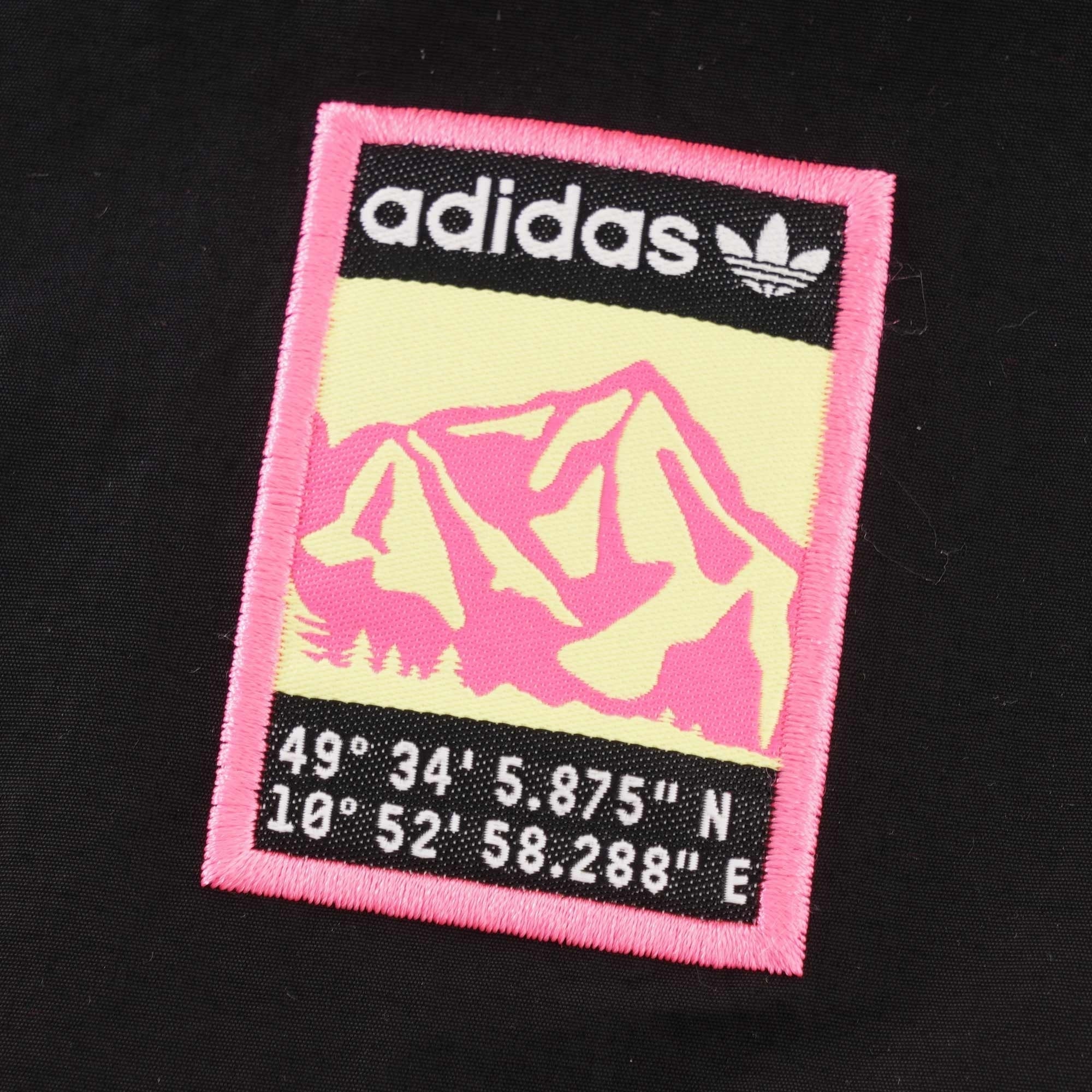 A close-up of the Adidas mountain logo on the black jacket, with coordinates below it.