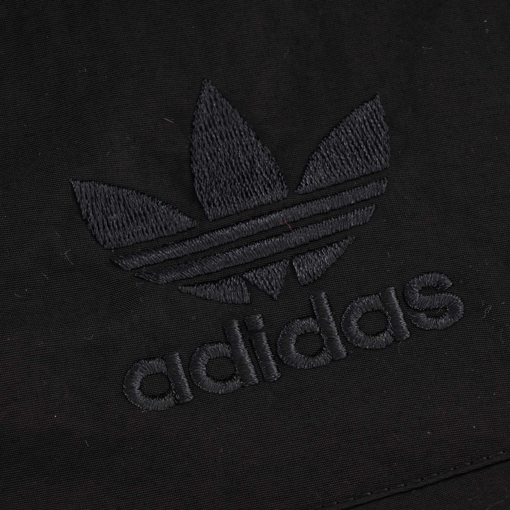 A close-up of the black embroidered Adidas logo on the black jacket.