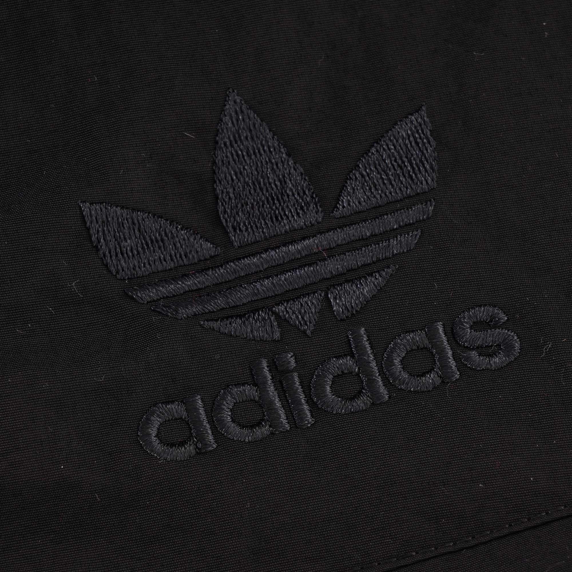 A close-up of the black embroidered Adidas logo on the black jacket.