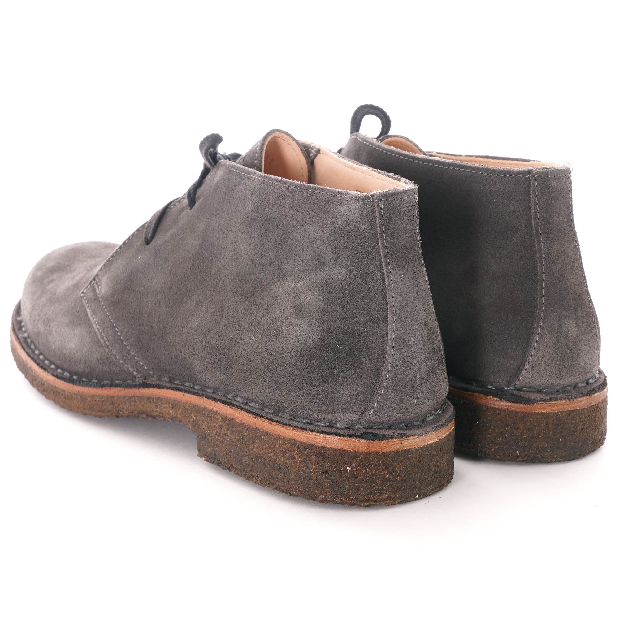 Rear view of a pair of grey suede desert boots with brown soles.