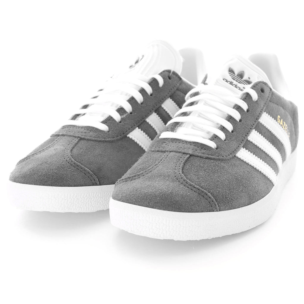 Pair of grey Adidas Gazelle trainers with white stripes and soles, angled forward.