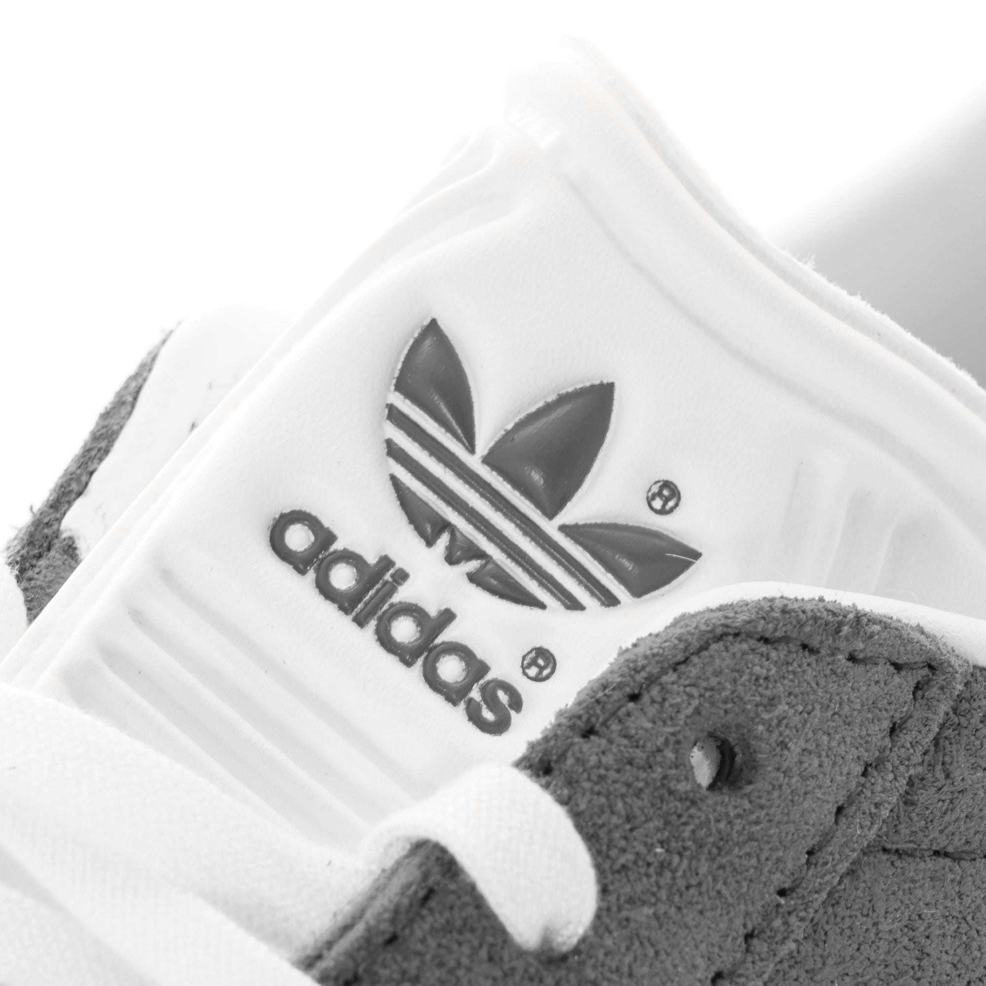Close-up of the Adidas logo on the white tongue of a grey Gazelle trainer.