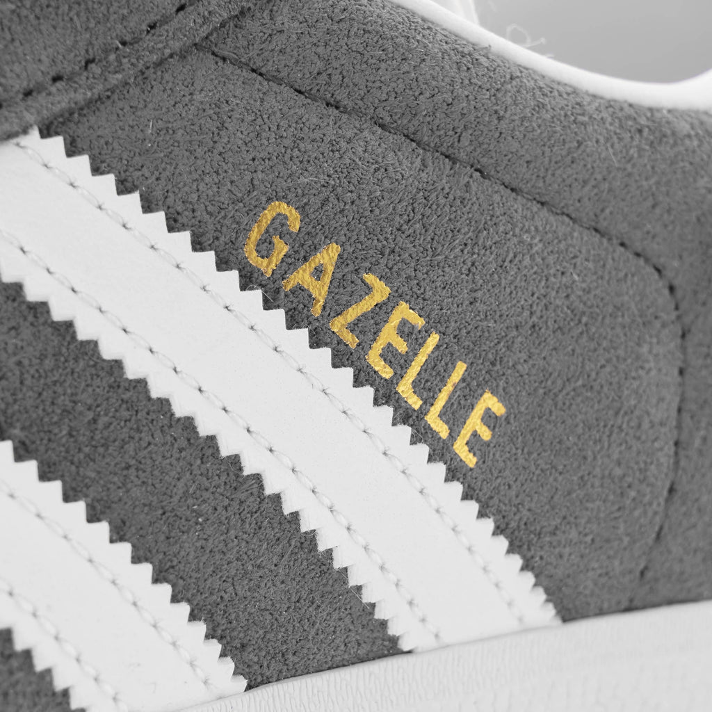 Close-up of the gold 'GAZELLE' text and white stripes on a grey trainer.