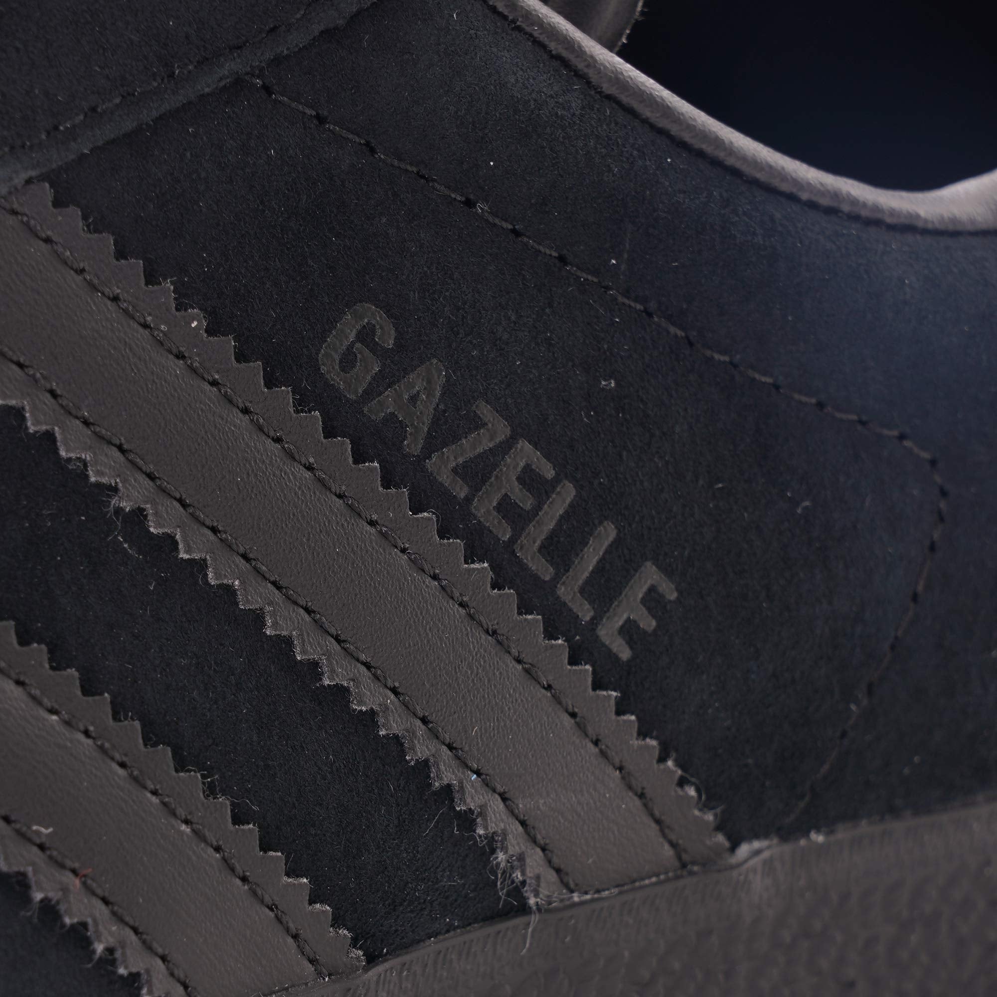 A close-up of the 'Gazelle' branding on the side of a black Adidas trainer.
