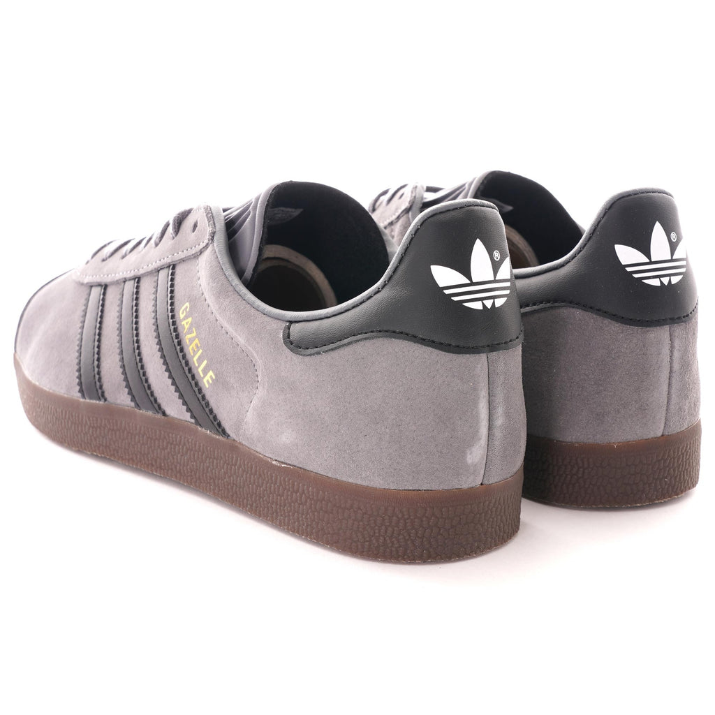 The rear view of two grey Adidas Gazelle trainers, showing the black heel tabs with white logos.