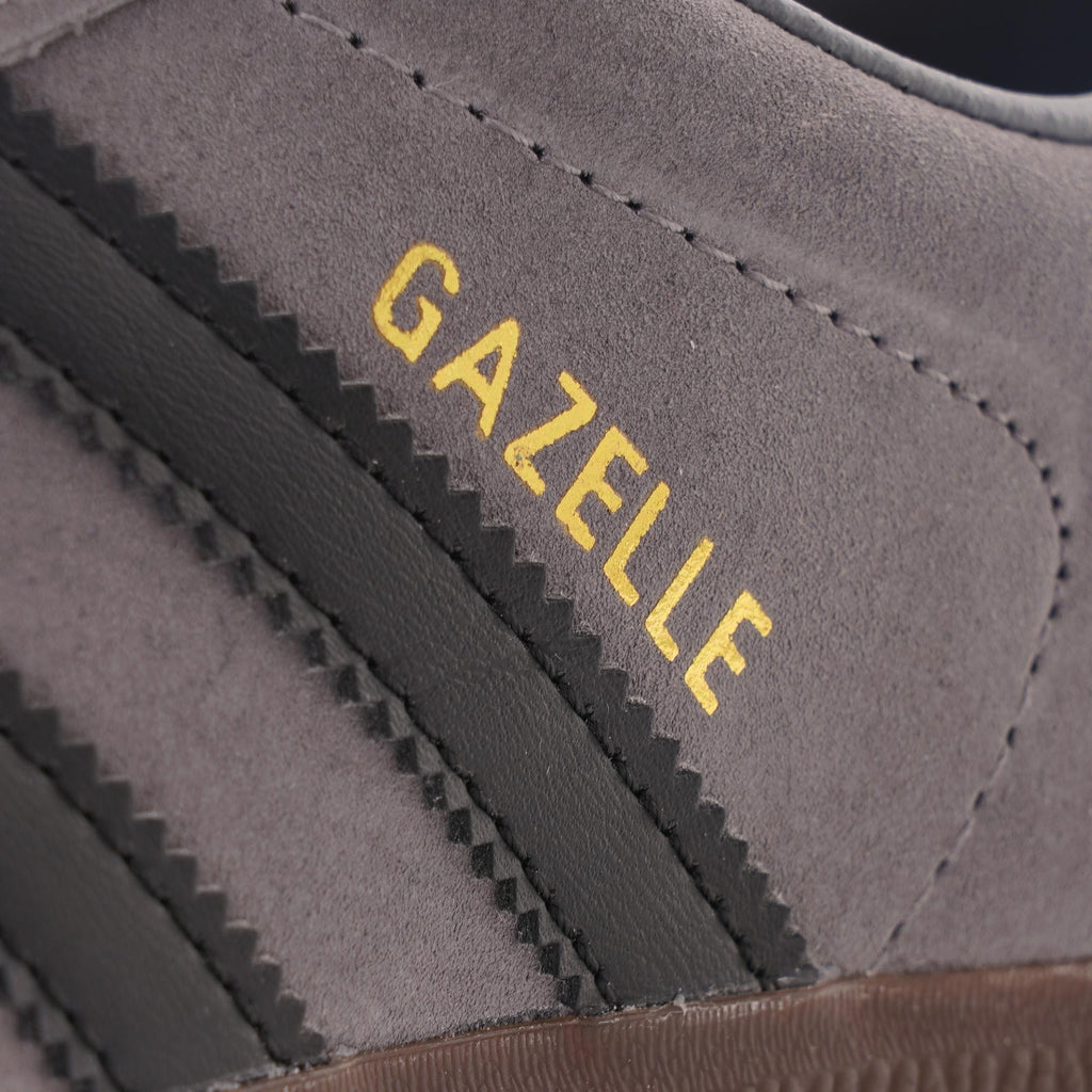 A close-up of the 'GAZELLE' text and black stripes on the side of a grey Adidas trainer.