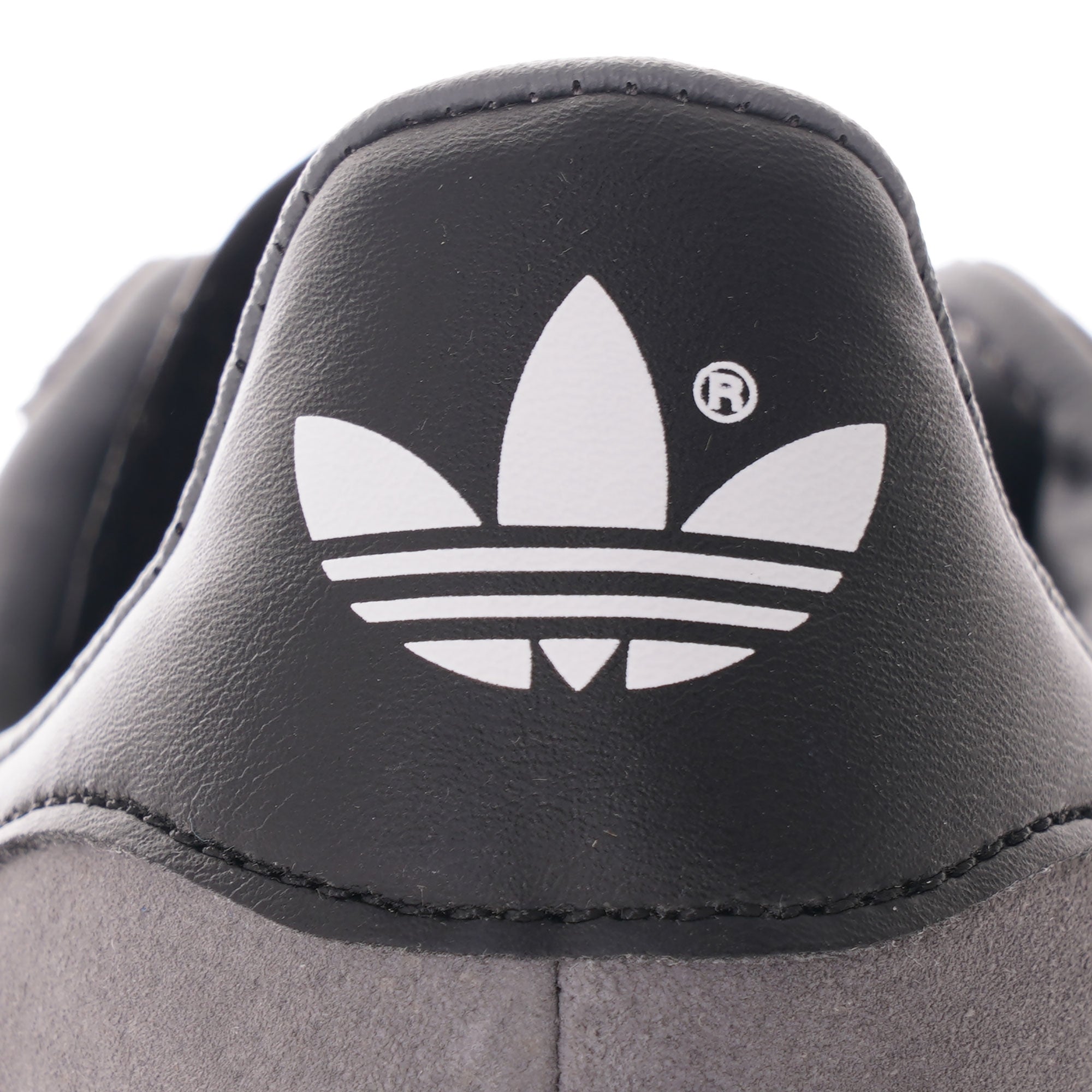 A close-up of the black heel tab with a white Adidas logo on a grey Gazelle trainer.